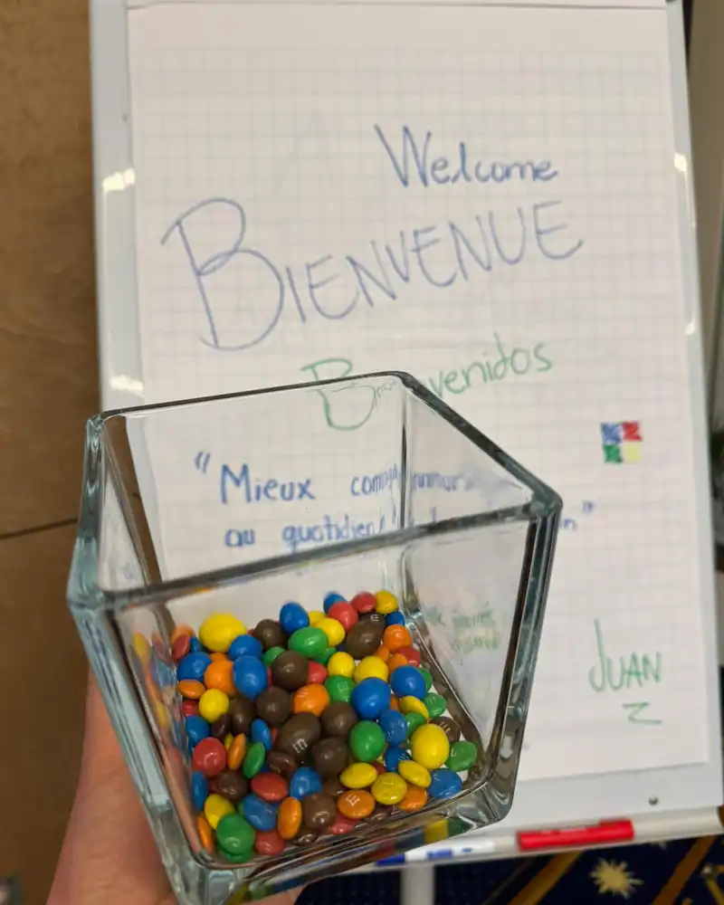 Glass geometric bowl filled with colorful candy being held in front of a hand-written 'Bienvenue / Welcome' sign.