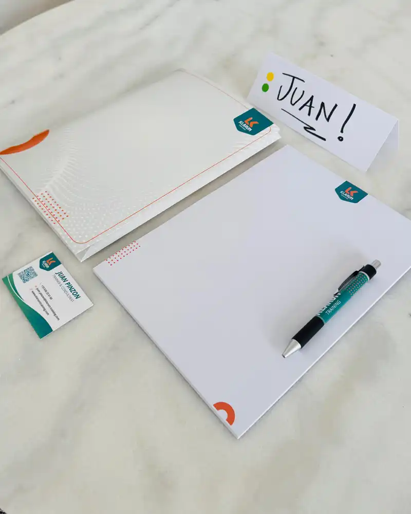 Name tag reading JUAN! placed beside a pen and white notebooks on a marble desk surface.